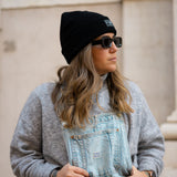 Black Beanie from It's okay | made in Portugal with love | feel cozy and warm with this knitted beanie. Pt gorro de inverno it's okay em preto. Image: woman wearing jeans overalls, a jacket on her waist and the black waffle beanie