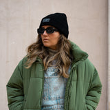 Black Beanie from It's okay | made in Portugal with love | feel cozy and warm with this knitted beanie. Pt gorro de inverno it's okay em preto. Image: woman looking left with sunglasses wearing black waffle beanie