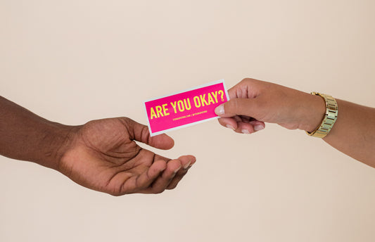 Are you okay? Join our self-love movement. Image: A female white hand giving a Are you okay sticker to a black hand. 