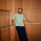 Man in a striped shirt standing, with wooden walls.