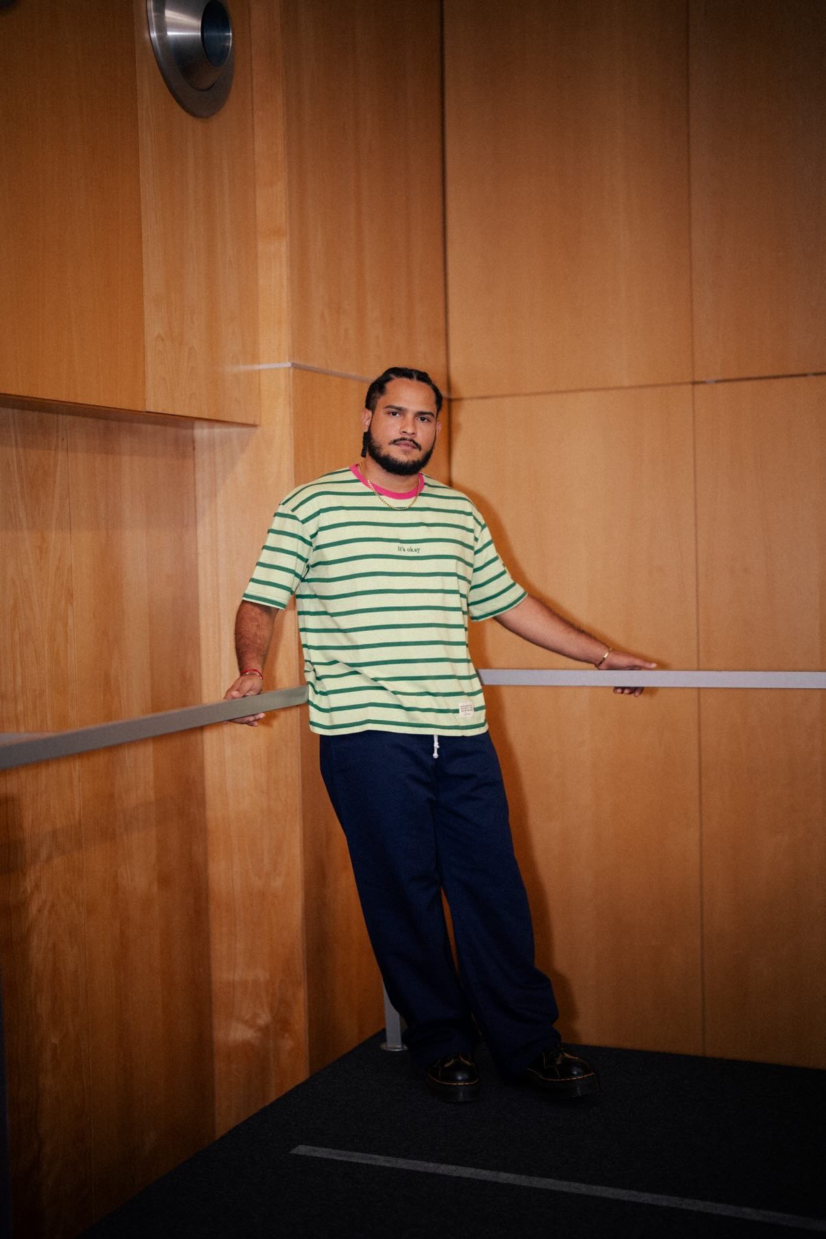 Man in a striped shirt standing, with wooden walls.