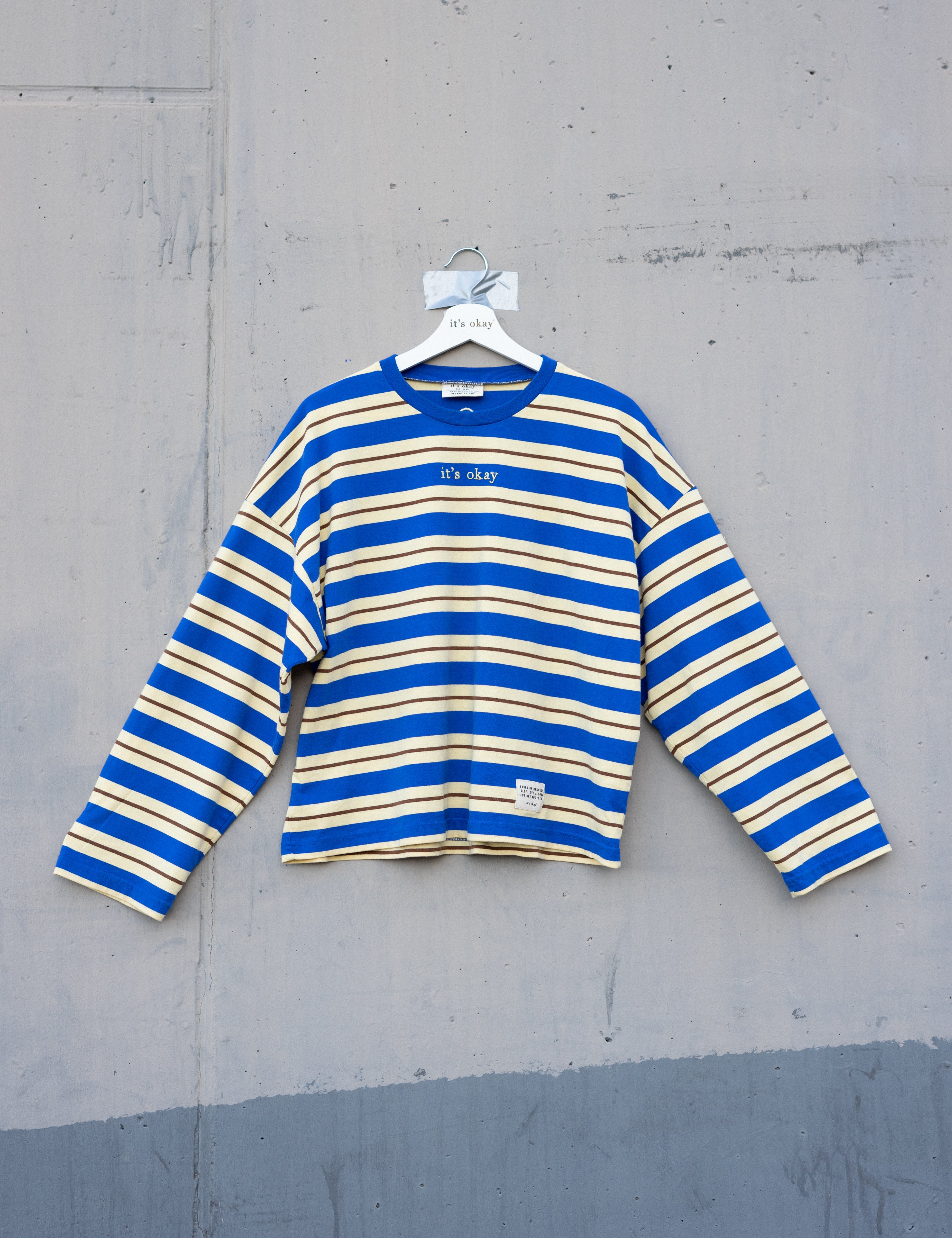 Blue and yellow striped shirt on a hanger against a gray concrete wall.