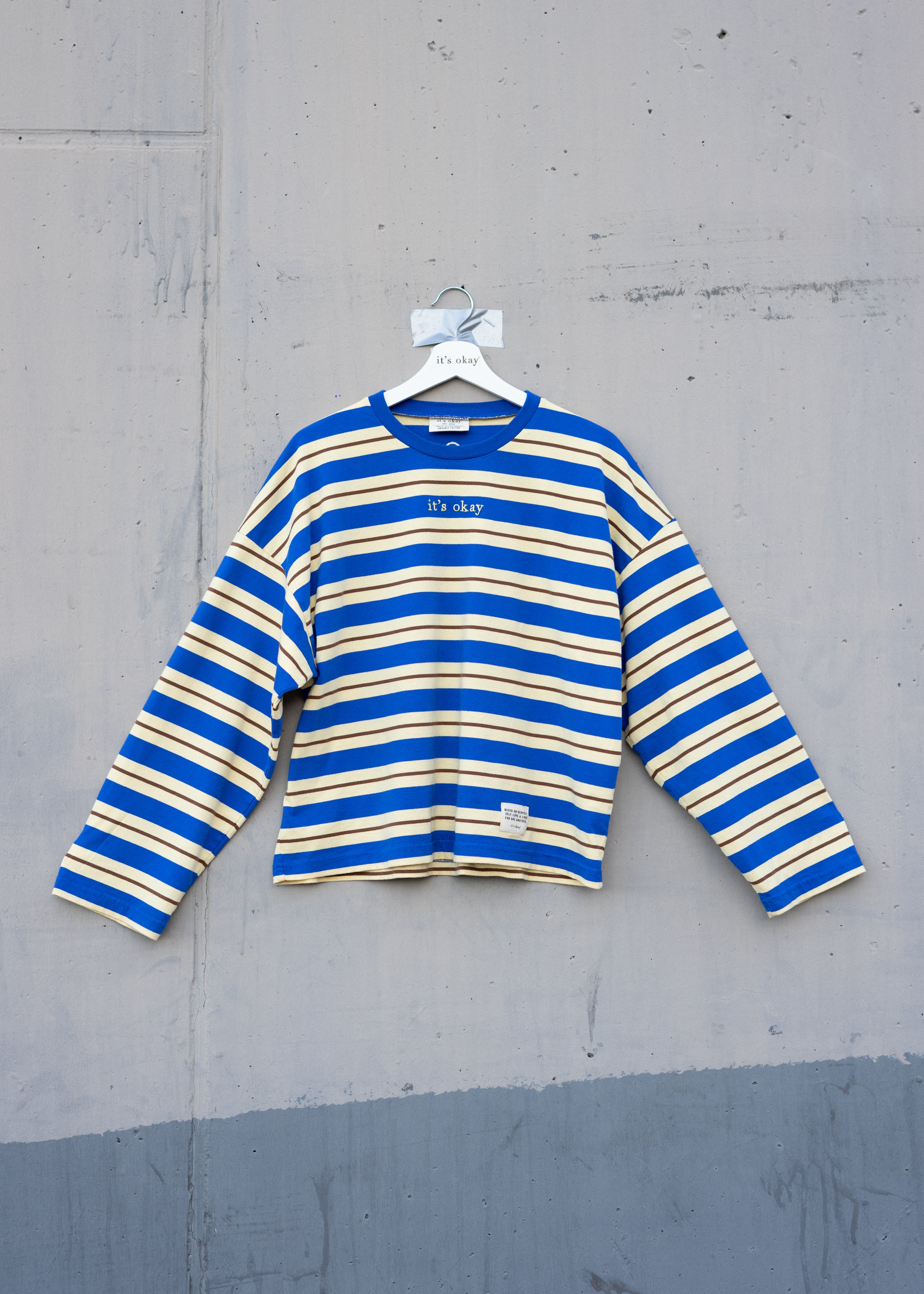 Blue and yellow striped shirt on a hanger against a gray concrete wall.