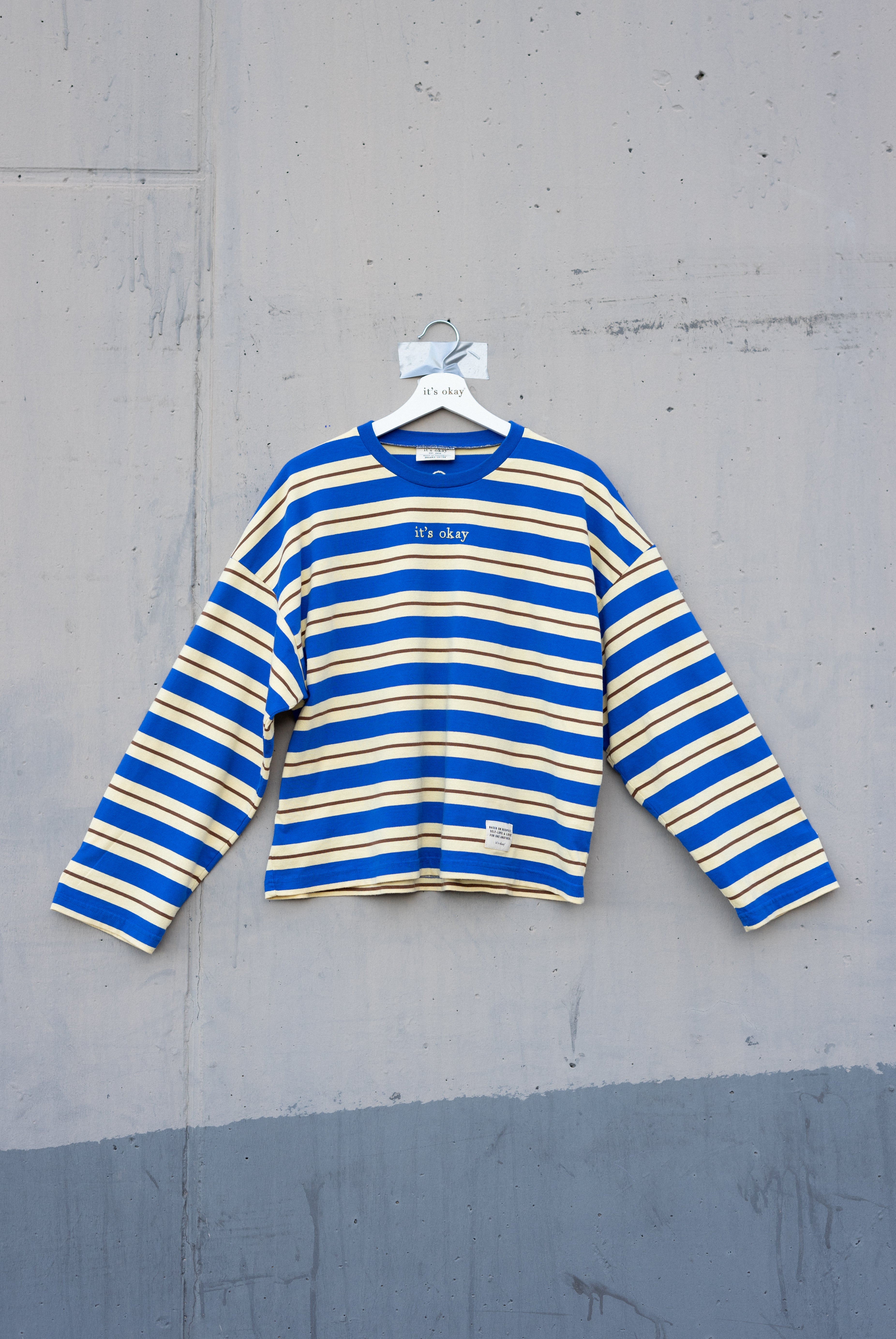 Blue and yellow striped shirt on a hanger against a gray concrete wall.