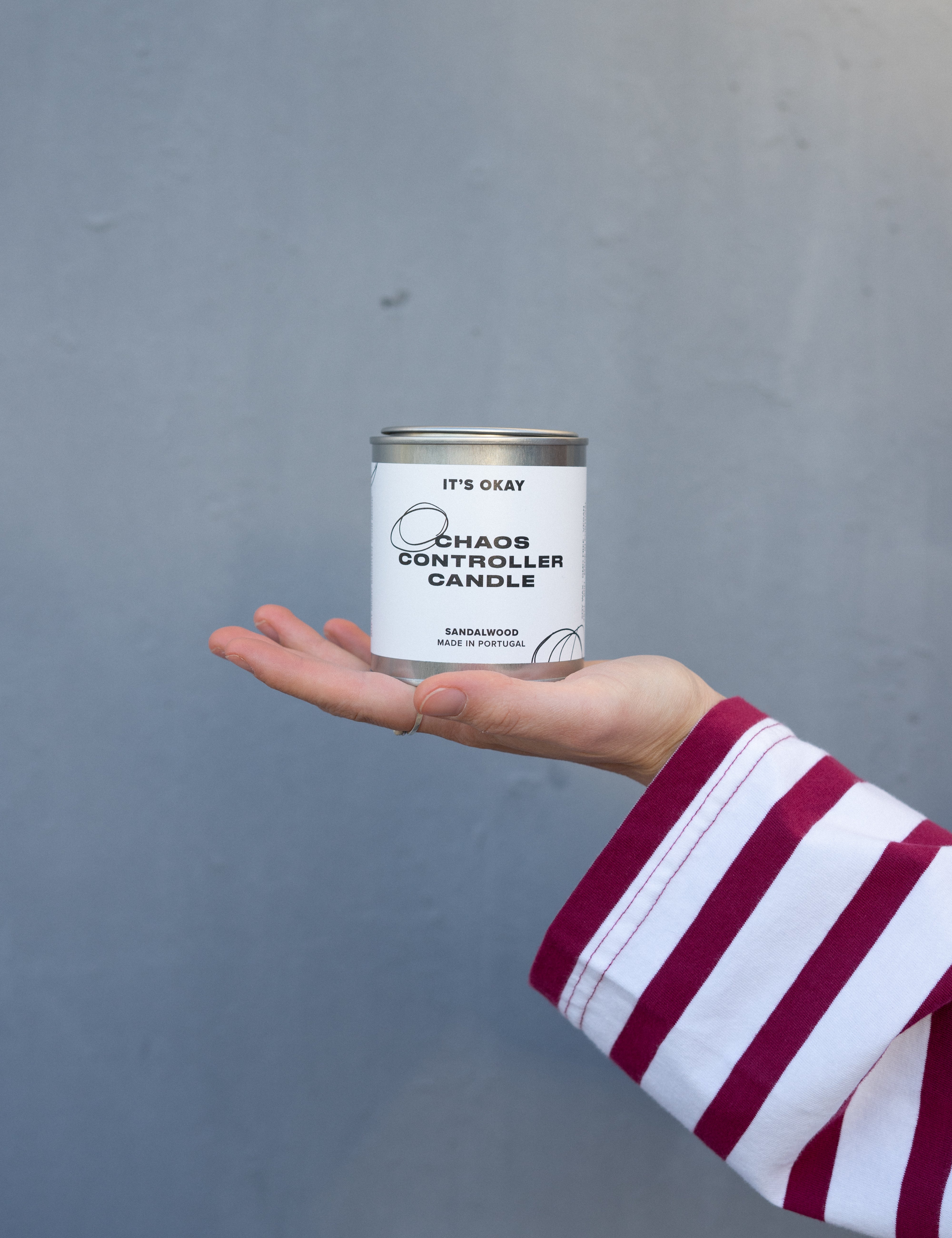 Hand holding a 'Chaos Controller Candle' can against a gray background