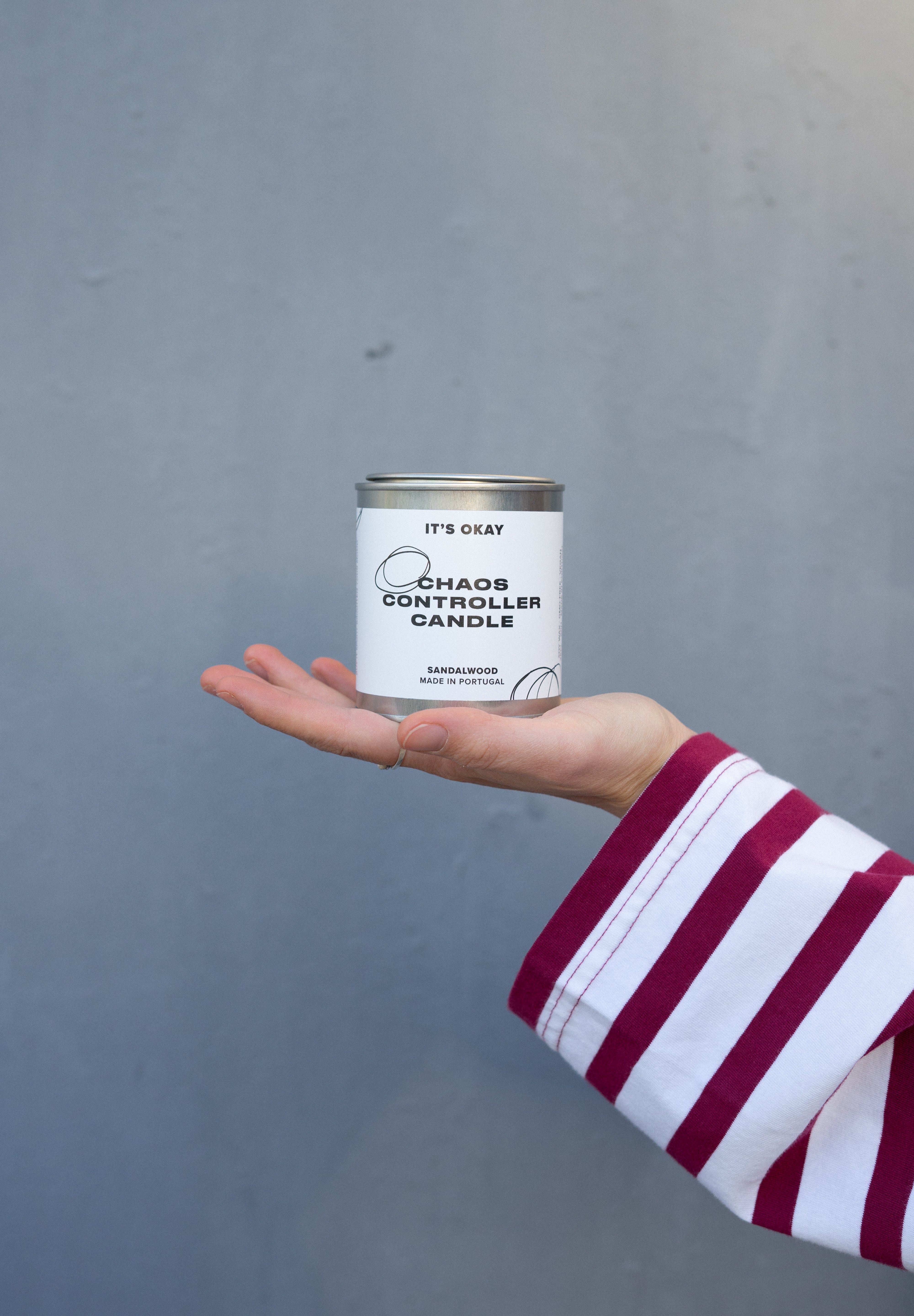 Hand holding a 'Chaos Controller Candle' can against a gray background