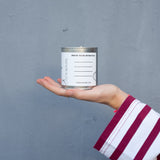 Hand holding a can of white paint against a gray background. Write your intention.