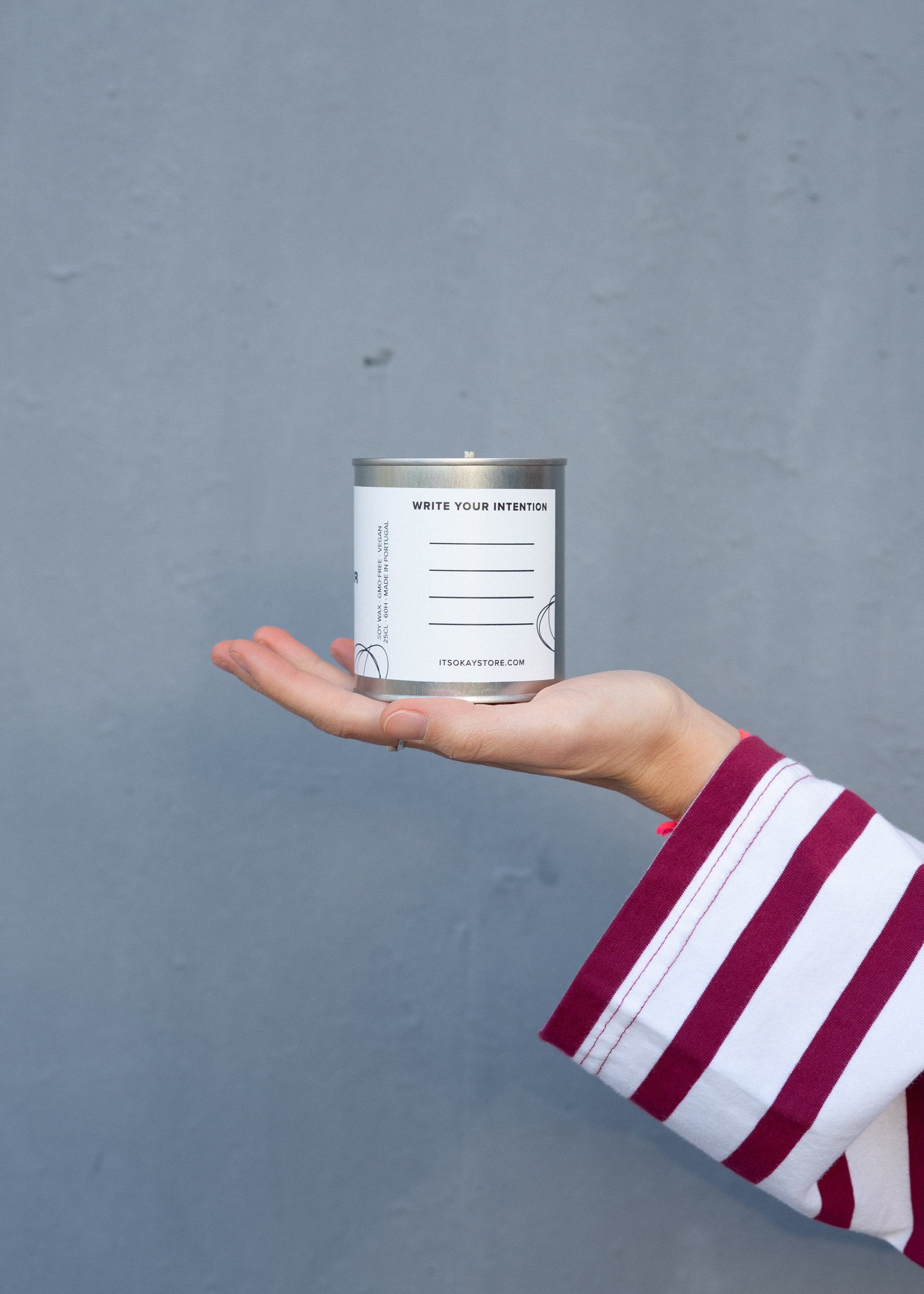 Hand holding a can of white paint against a gray background. Write your intention.