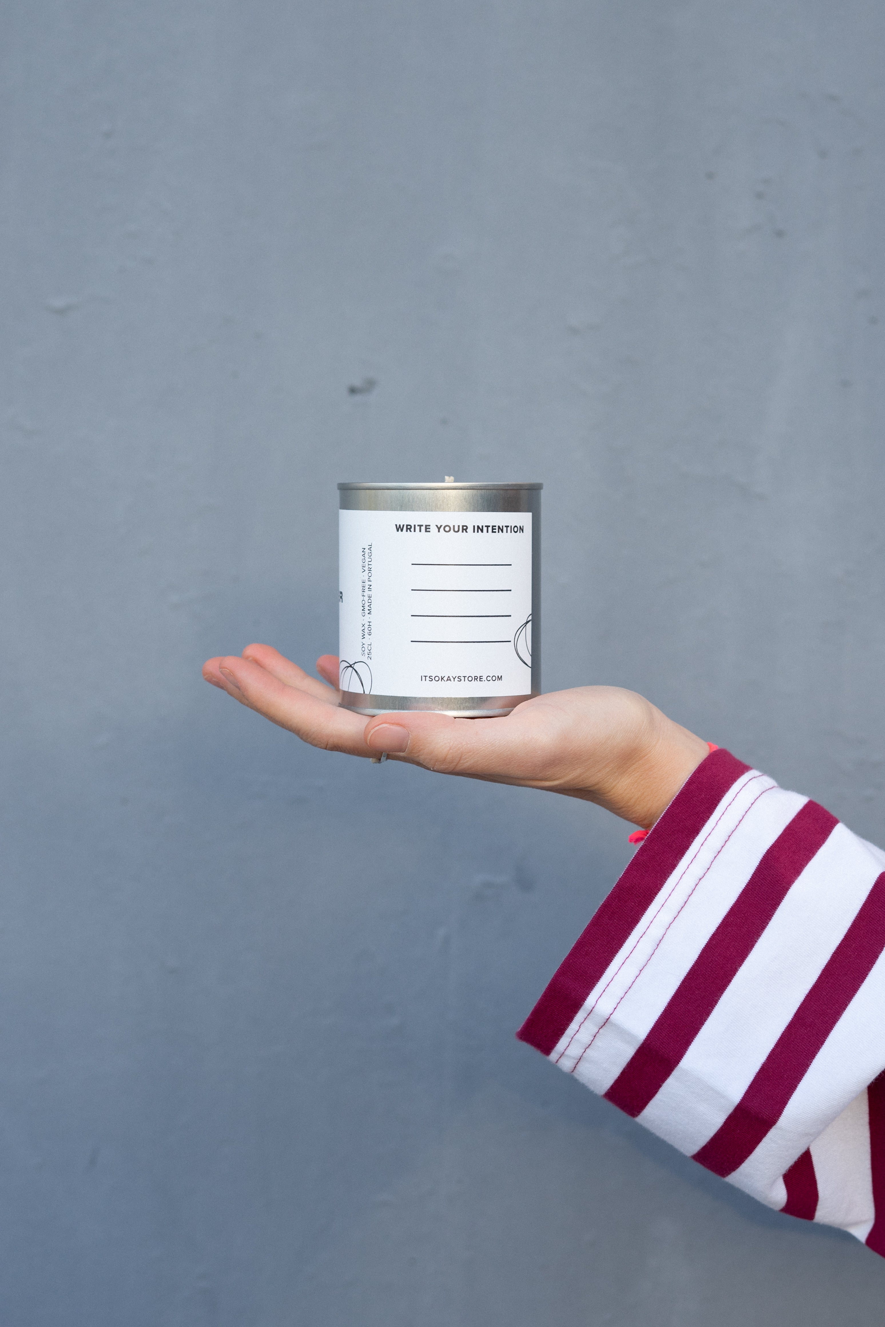 Hand holding a can of white paint against a gray background. Write your intention.