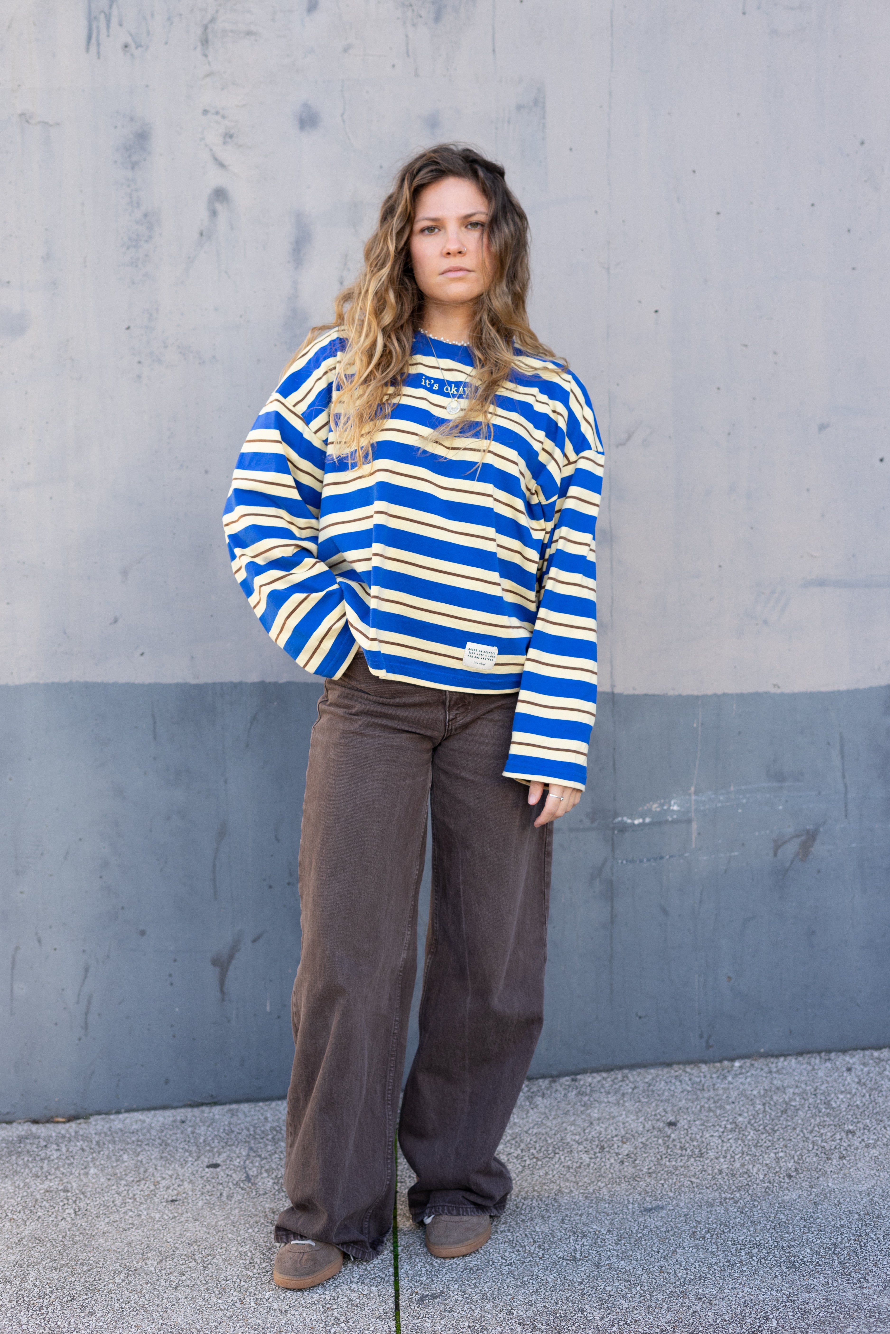 Woman wearing a blue and yellow striped sweater against a gray wall.