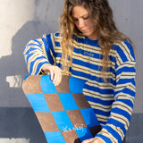 Woman holding a checkered skateboard with 'it's okay' text against a gray wall.