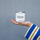Hand holding a can labeled 'Mental Breakdown Candle' against a gray background