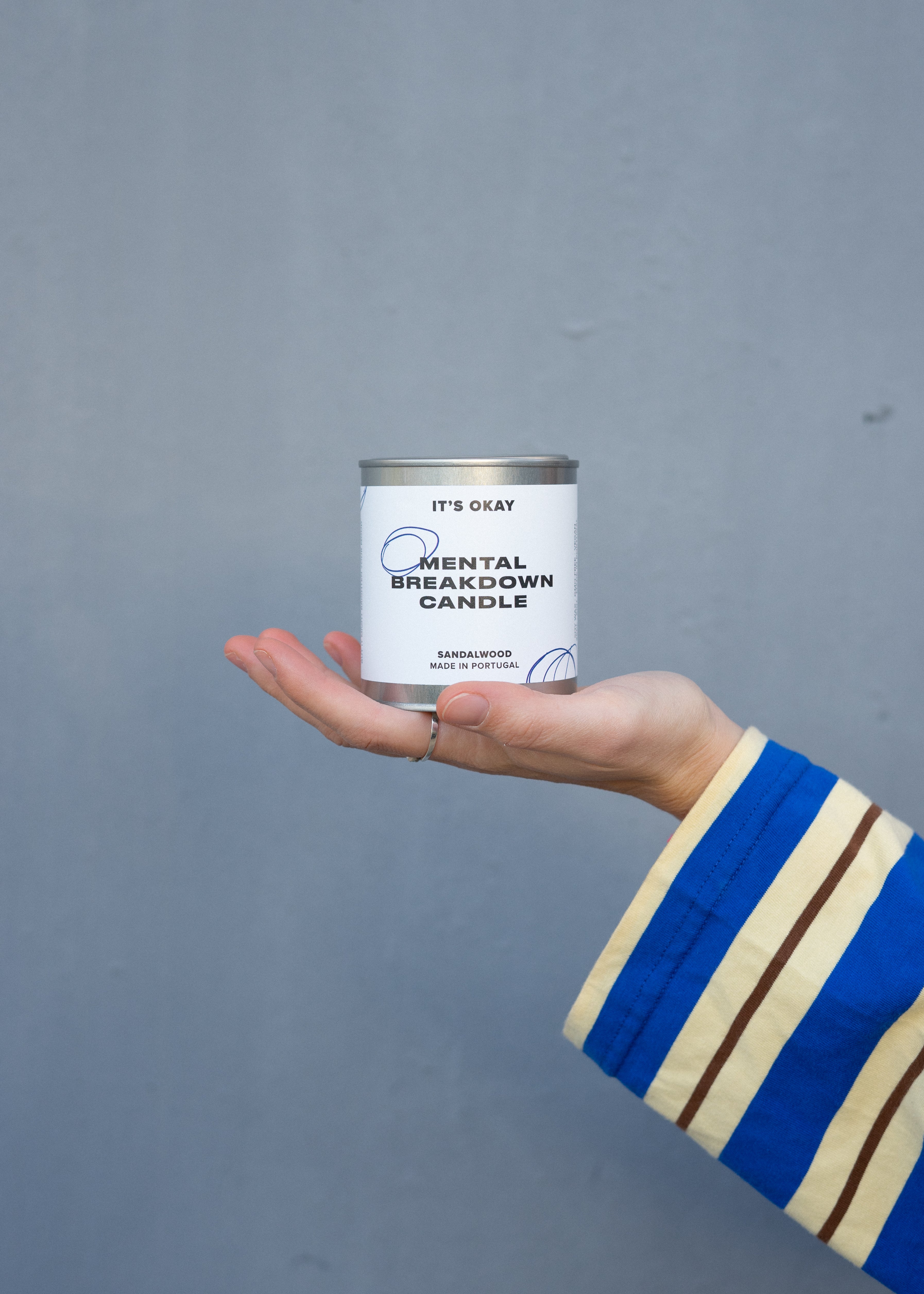 Hand holding a can labeled 'Mental Breakdown Candle' against a gray background