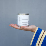 Hand holding a small can with a label against a gray background. Write your intentions.