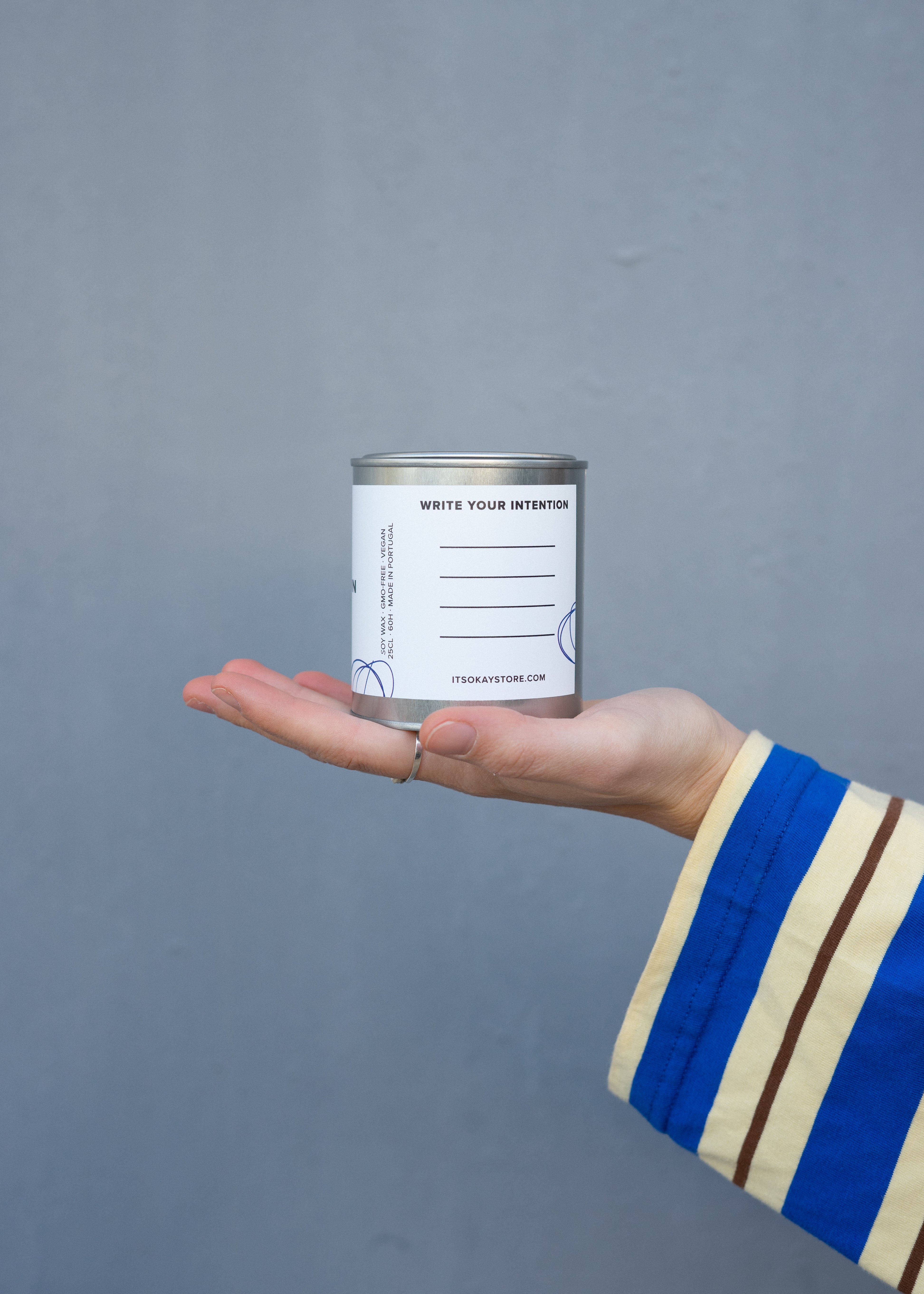 Hand holding a small can with a label against a gray background. Write your intentions.