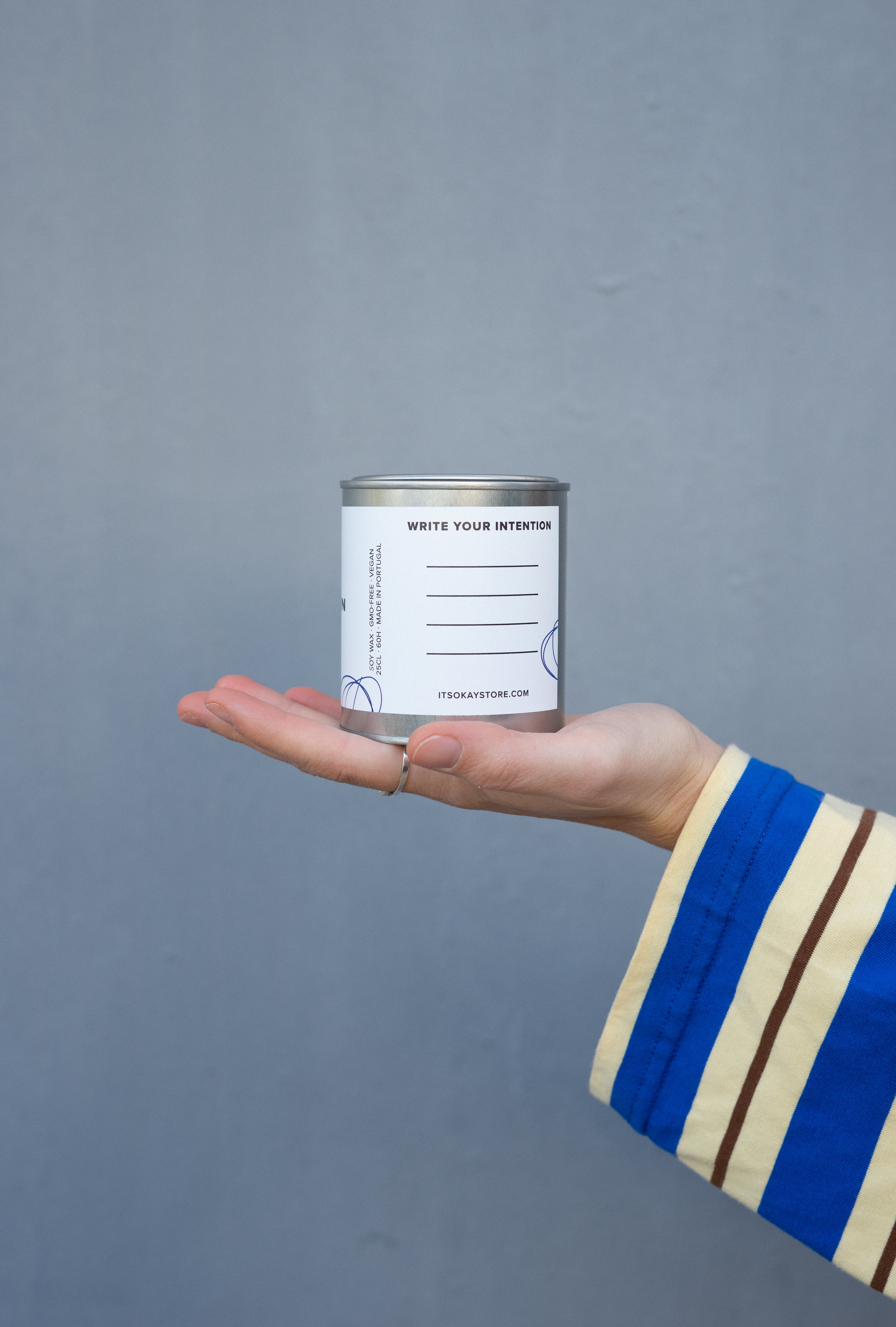 Hand holding a small can with a label against a gray background. Write your intentions.