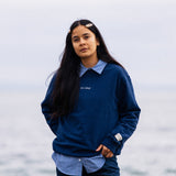 Woman wearing navy IT’S OKAY organic cotton crewneck outdoors by the sea, relaxed fit.
