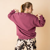 Back view of model wearing burgundy IT’S OKAY organic cotton crewneck, showing embroidered circle detail.
