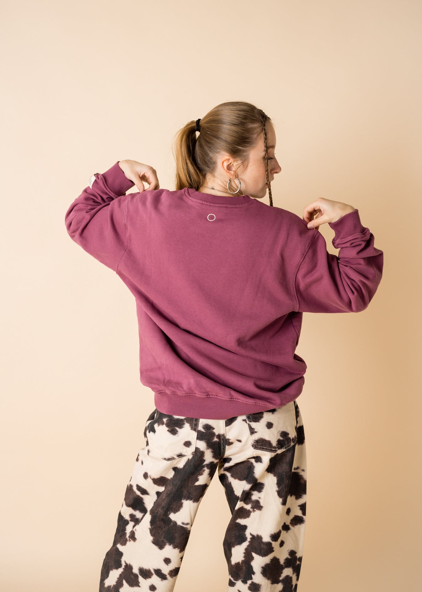Back view of model wearing burgundy IT’S OKAY organic cotton crewneck, showing embroidered circle detail.
