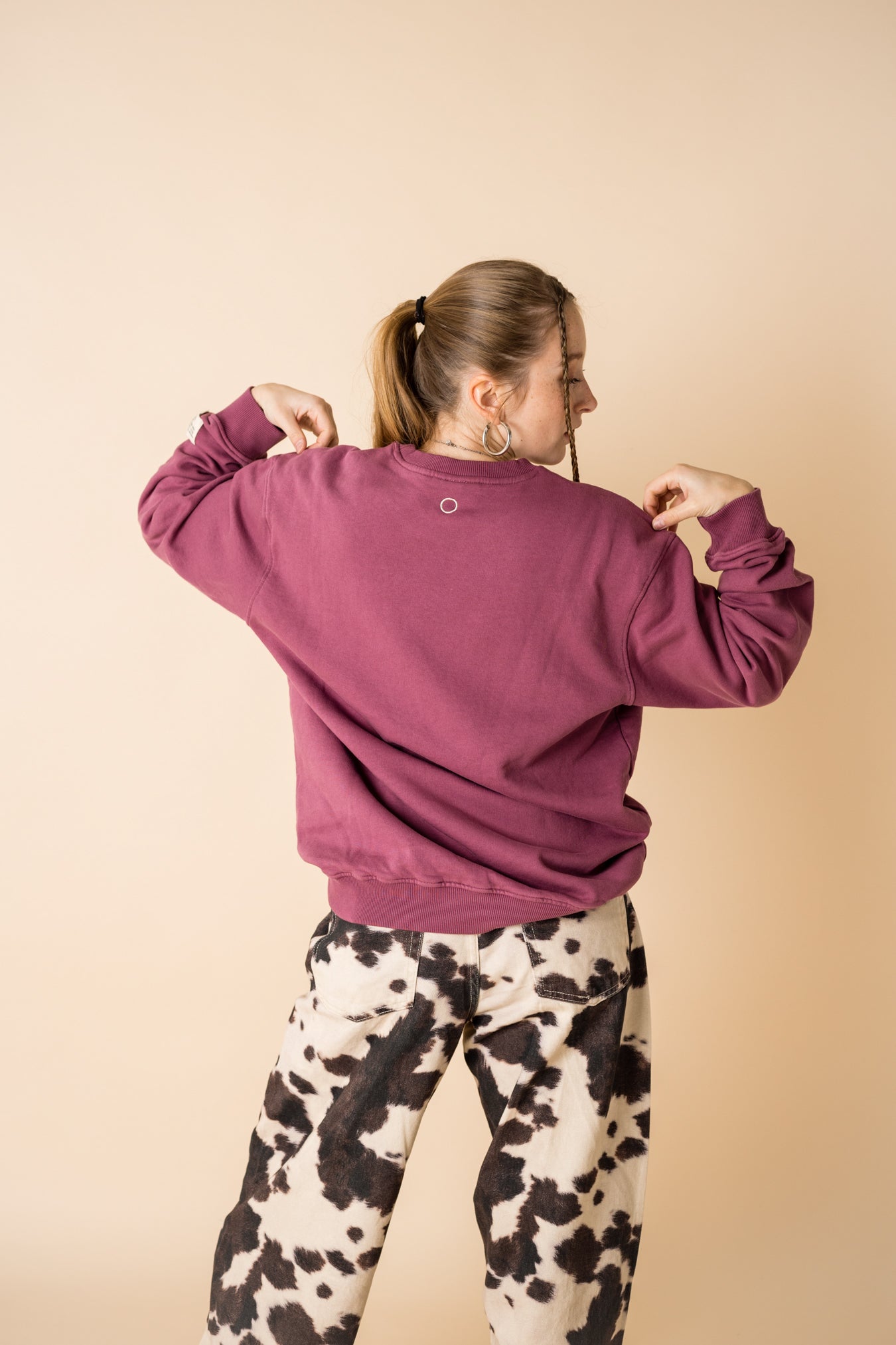 Back view of model wearing burgundy IT’S OKAY organic cotton crewneck, showing embroidered circle detail.