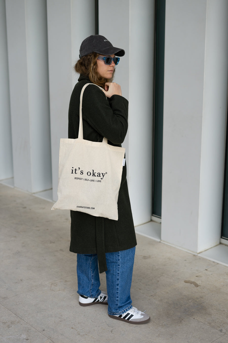 it's okay tote bag: organic cotton with black ink. Photo: girl with long coat and blackberry it's okay cap wearing the tote bag