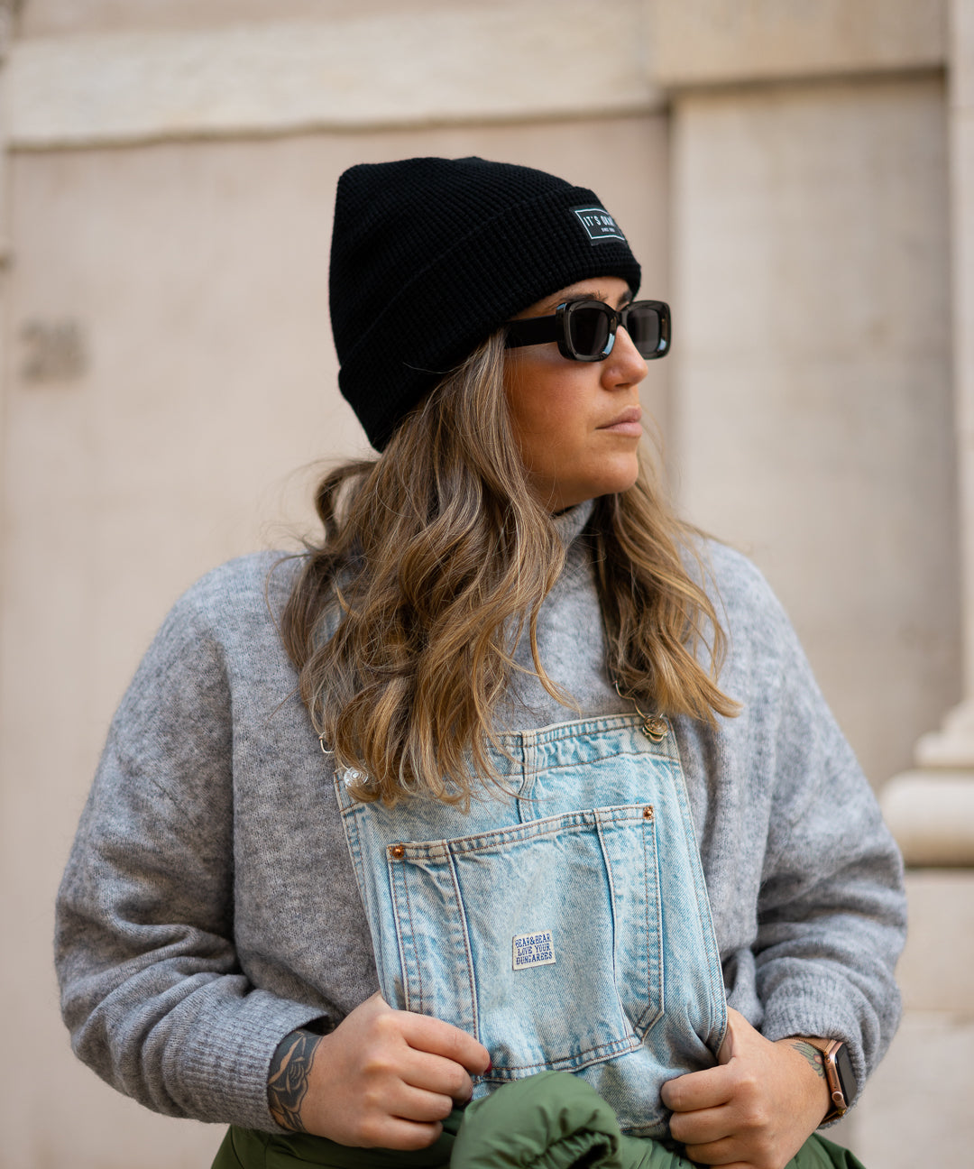 Black Beanie from It's okay | made in Portugal with love | feel cozy and warm with this knitted beanie. Pt gorro de inverno it's okay em preto. Image: woman wearing jeans overalls, a jacket on her waist and the black waffle beanie 