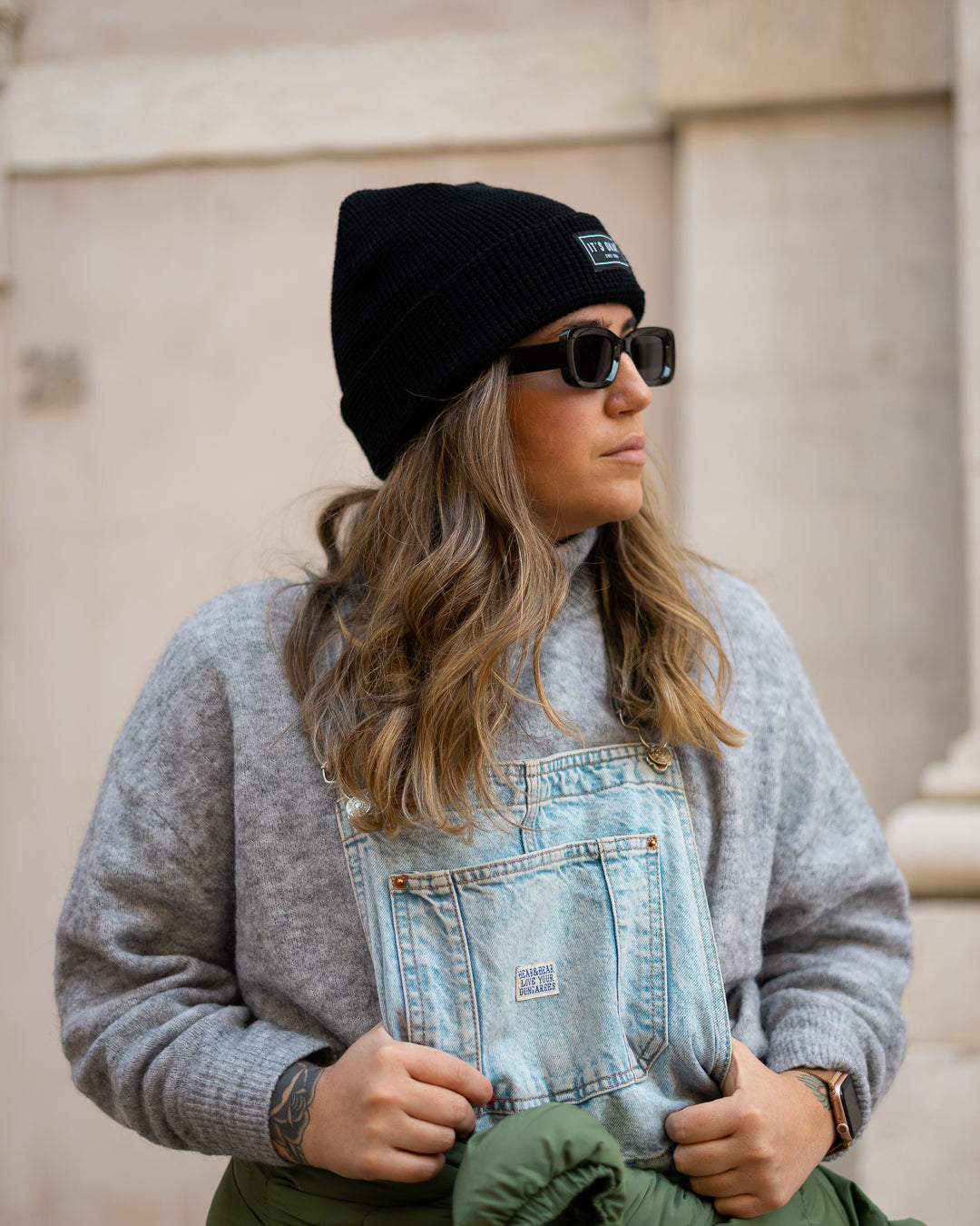 Black Beanie from It's okay | made in Portugal with love | feel cozy and warm with this knitted beanie. Pt gorro de inverno it's okay em preto. Image: woman wearing jeans overalls, a jacket on her waist and the black waffle beanie 