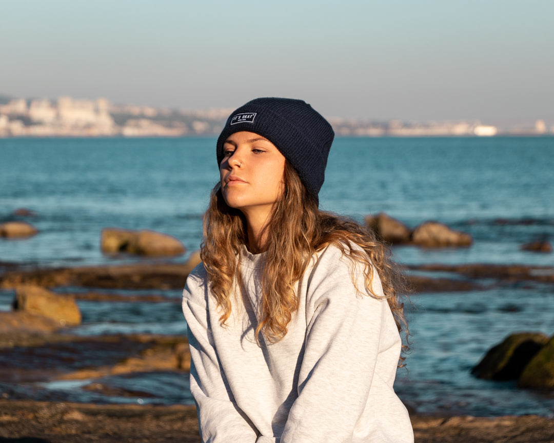 Blue Beanie from It's okay | design in Portugal with love | feel cozy and warm with this knitted beanie | gorro feito em Portugal, wear it with pride. Image: woman wearing blue waffle beanie with the sea behind her. 