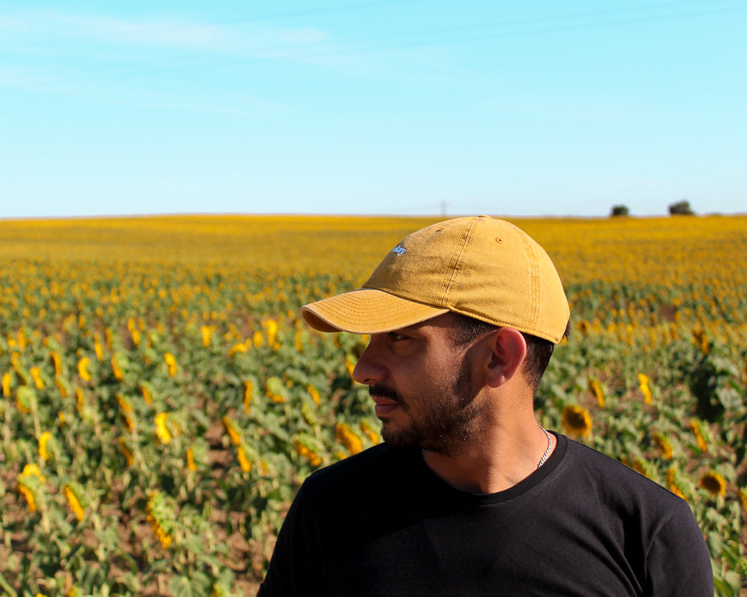Sunflower cap, yellow cap made with 100% cotton, embroidered. it's okay to be exactly who you are. From Portugal with love. Boné de pala amarelo de algodão bordado em Portugal. Photography: Men with beard in a sunflower field wearing sunflower cap