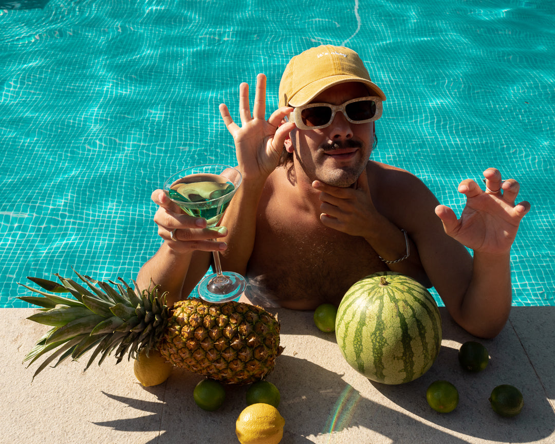 Sunflower cap, yellow cap made with 100% cotton, embroidered. it's okay to be exactly who you are. From Portugal with love. Boné de pala amarelo de algodão bordado em Portugal. Image: Mustache man in a pool with a martini drink and fruit wearing the sunflower cap. 